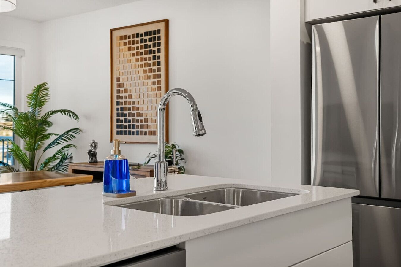 A modern kitchen with a stainless steel refrigerator, a double sink, and a decorative wall piece.