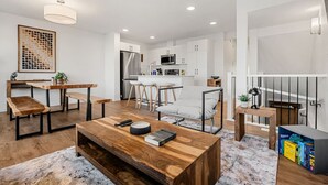A modern living room with a wooden coffee table, a sofa, and a dining area with a kitchen in the background. - Luxury Family Retreat w/ Games, King Bed & Garage (Edmonton)