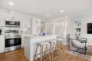 Una cocina moderna con electrodomésticos de acero inoxidable, una isla blanca con taburetes y una escalera que lleva a un nivel superior.