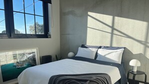 Et soveværelse med en seng, et billede i ramme, en radiator, en lampe og et vindue med havudsigt.