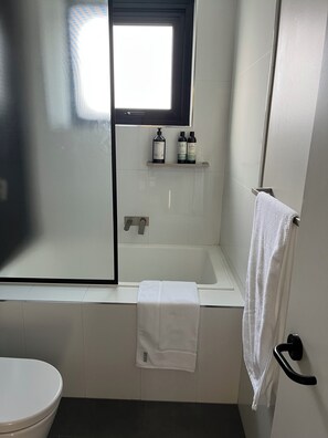 A bathroom with a bathtub, a toilet, a window, and a towel rack. - Luxurious 2 Bed 2 Bath Woolstore apartment (Kingston)