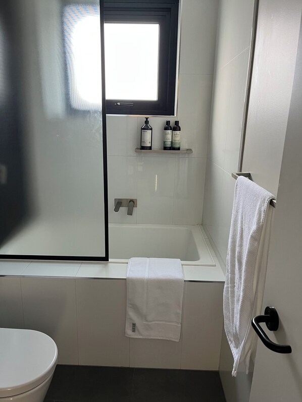 Un baño con bañera, inodoro, ventana y perchero para toallas.
