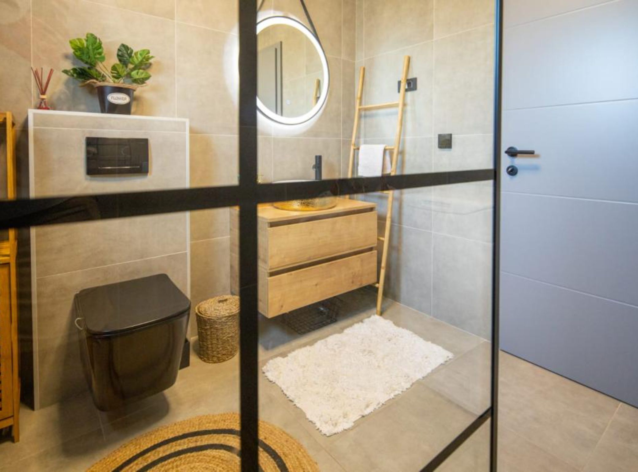 Een moderne badkamer met een glazen douchecabine, een houten wastafelmeubel en een kleine potplant.