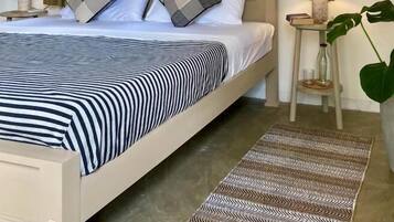 A neatly made bed with striped bedding, two bedside lamps, a window with curtains, and a patterned rug.