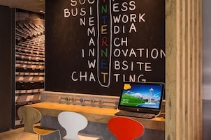A reception desk with a laptop, a blackboard with words like 'BUSINESS,' 'INTERNET,' and 'CHAT,' and a seating area with chairs.