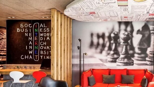 Un intérieur moderne agrémenté d’une fresque murale représentant un échiquier, d’un canapé rouge et d’une bibliothèque en bois.