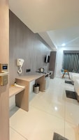 Habitación de hotel moderna con un escritorio de madera, un teléfono, un hervidor de agua, un televisor y una cama.