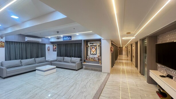 A modern living room with a sofa set, a flat-screen TV, and a hallway leading to other rooms. - Hotel Bluzill (Vadodara)