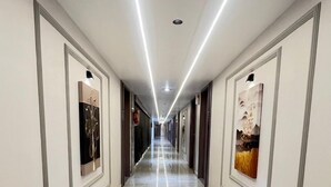 A long, well-lit hallway with marble flooring and framed artwork on the walls. - Hotel Bluzill (Vadodara)