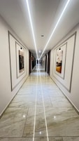 Un largo pasillo bien iluminado con suelo de mármol y cuadros enmarcados en las paredes.