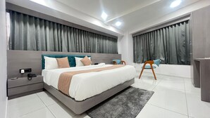 A modern bedroom with a large bed, bedside tables, a chair, and a bathroom with a bathtub. - Hotel Bluzill (Vadodara)