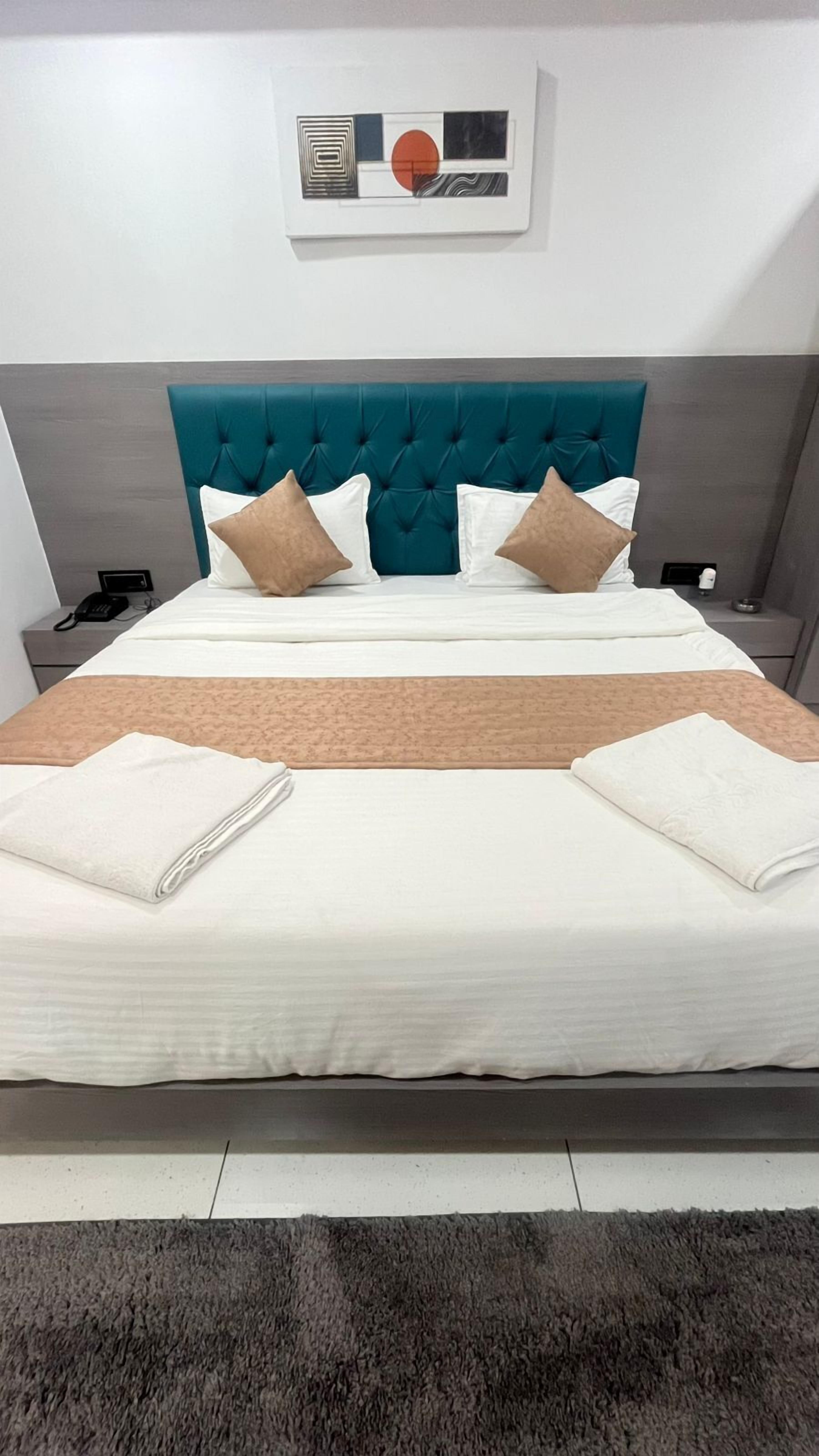 Een opgemaakt bed met een blauwgroen hoofdeinde, witte lakens en twee gevouwen handdoeken.