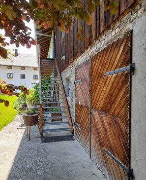 Eine Holztreppe führt zu einer großen Scheunentür, im Hintergrund ein weißes Gebäude.