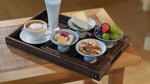 Ein Frühstücksbrett mit einer Kaffeetasse, einem Glas Milch, einer Scheibe Käsekuchen, einer Fruchtschale und einer Schale mit Nüssen.
