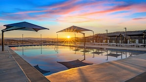 Ein Schwimmbecken mit Sonnenschirmen und Liegestühlen, umgeben von einem Zaun und Hügeln im Hintergrund.
