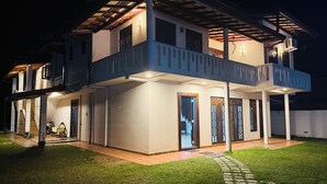 Uma casa de dois andares com varanda, alpendre coberto e gramado bem cuidado.