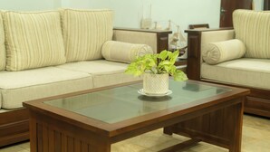 Uma sala de estar com um sofá bege, uma mesa de centro de vidro e uma planta decorativa.