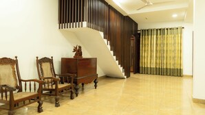 Ampla sala de estar com escada, cadeiras de madeira, um armário de madeira e um ventilador de teto.