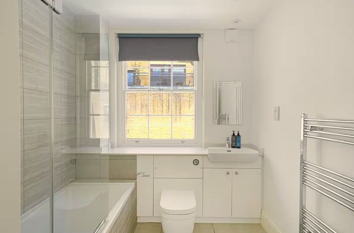 A compact bathroom with a bathtub, toilet, and sink, featuring a window with a view of the outside.
