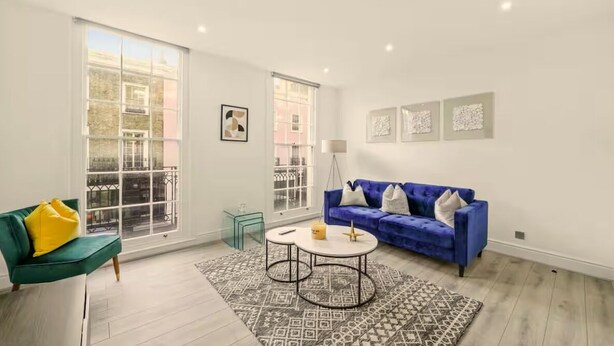 A modern living room with a green sofa, a blue sofa, and a patterned rug. - Flat 2 Beauchamp Place (London)