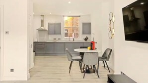A modern kitchen with grey cabinets, a central island, and a dining area with grey chairs. - Flat 2 Beauchamp Place (London)