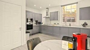 A modern kitchen with grey cabinets, a stainless steel range, and a window with a view of a brick building. - Flat 2 Beauchamp Place (London)