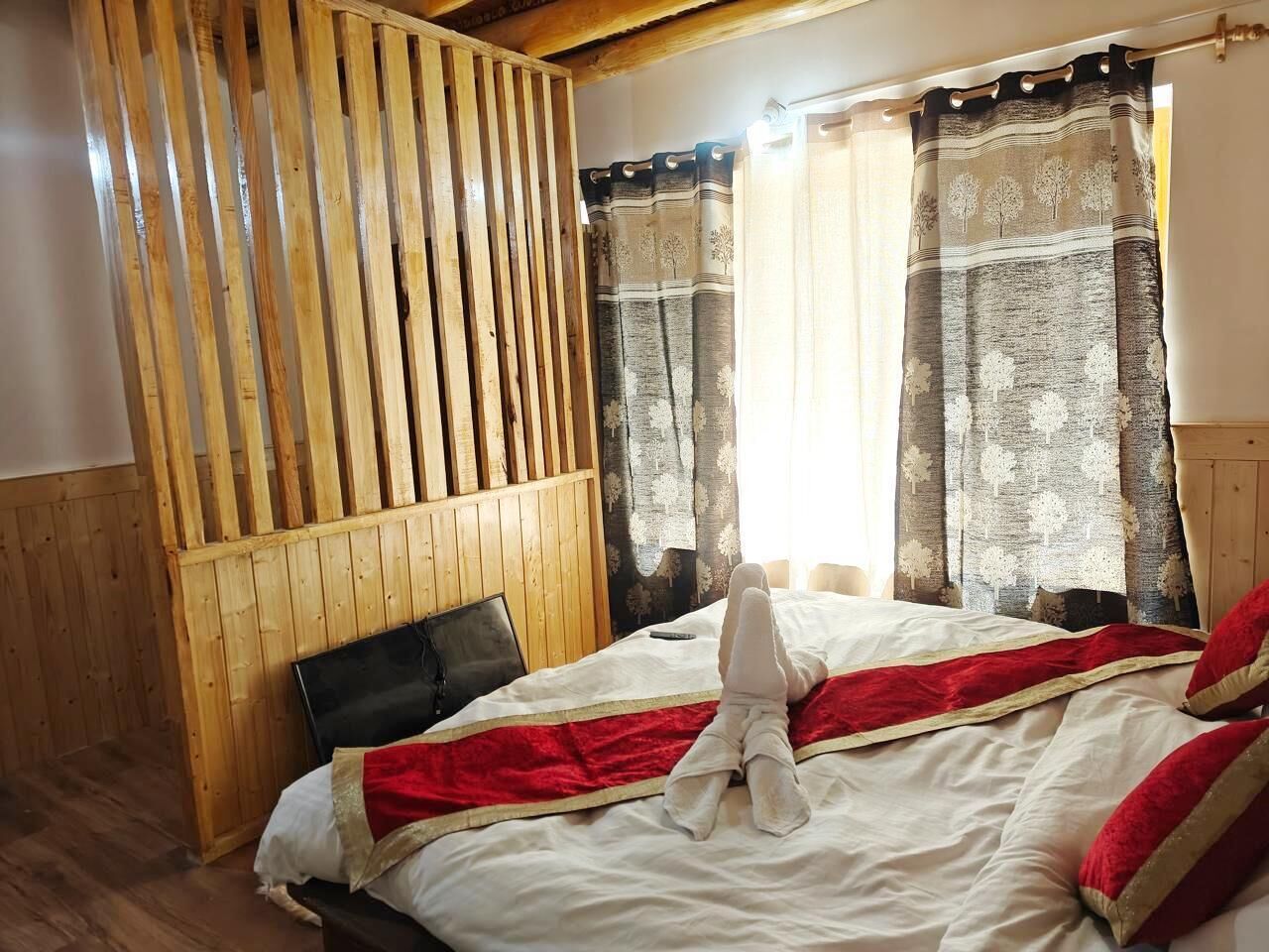 A bedroom with a wooden headboard, a bed with white and red bedding, and two curtains with tree patterns.