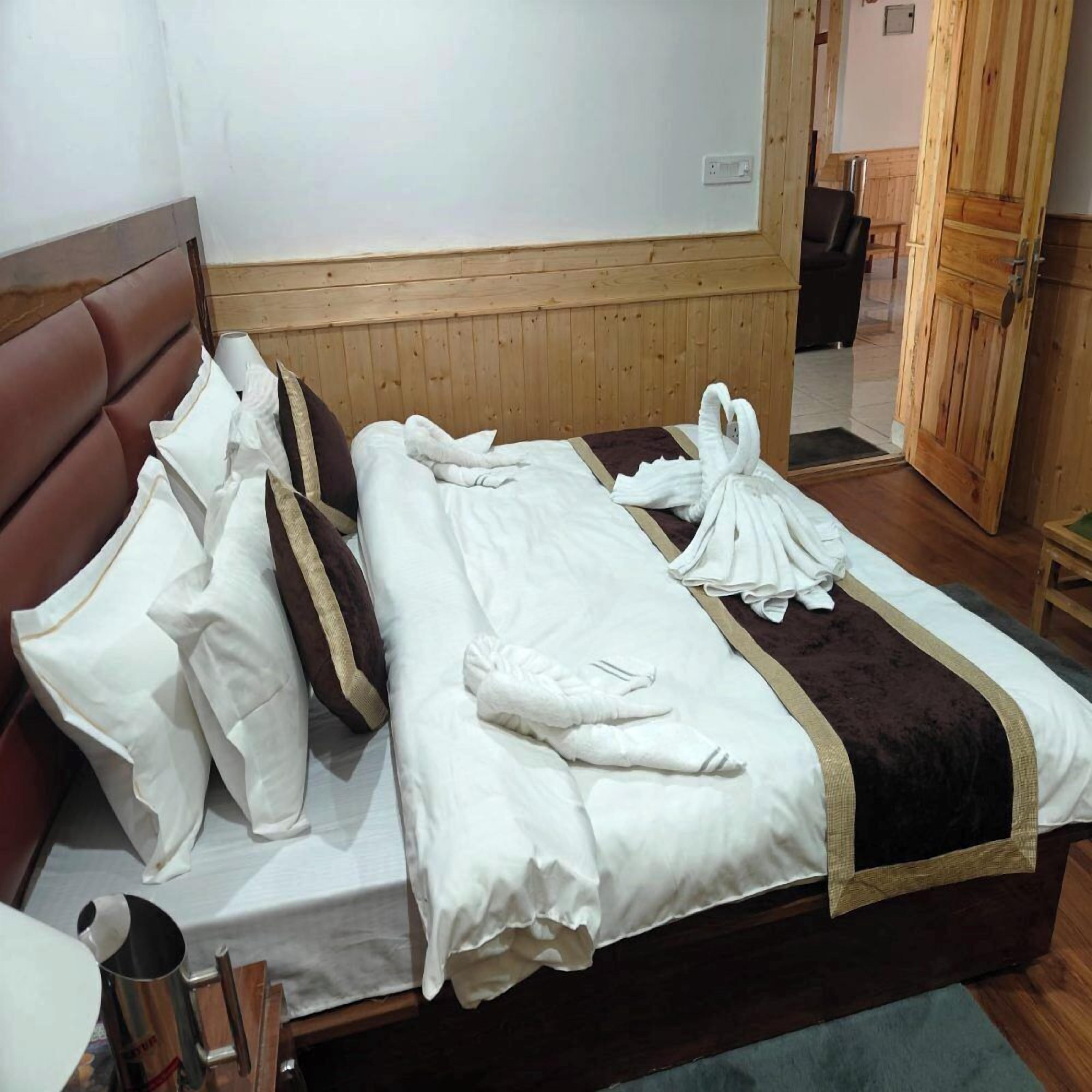 Una habitación de hotel con cabecera de madera, cama con ropa blanca y un detalle en marrón, y un armario de madera.