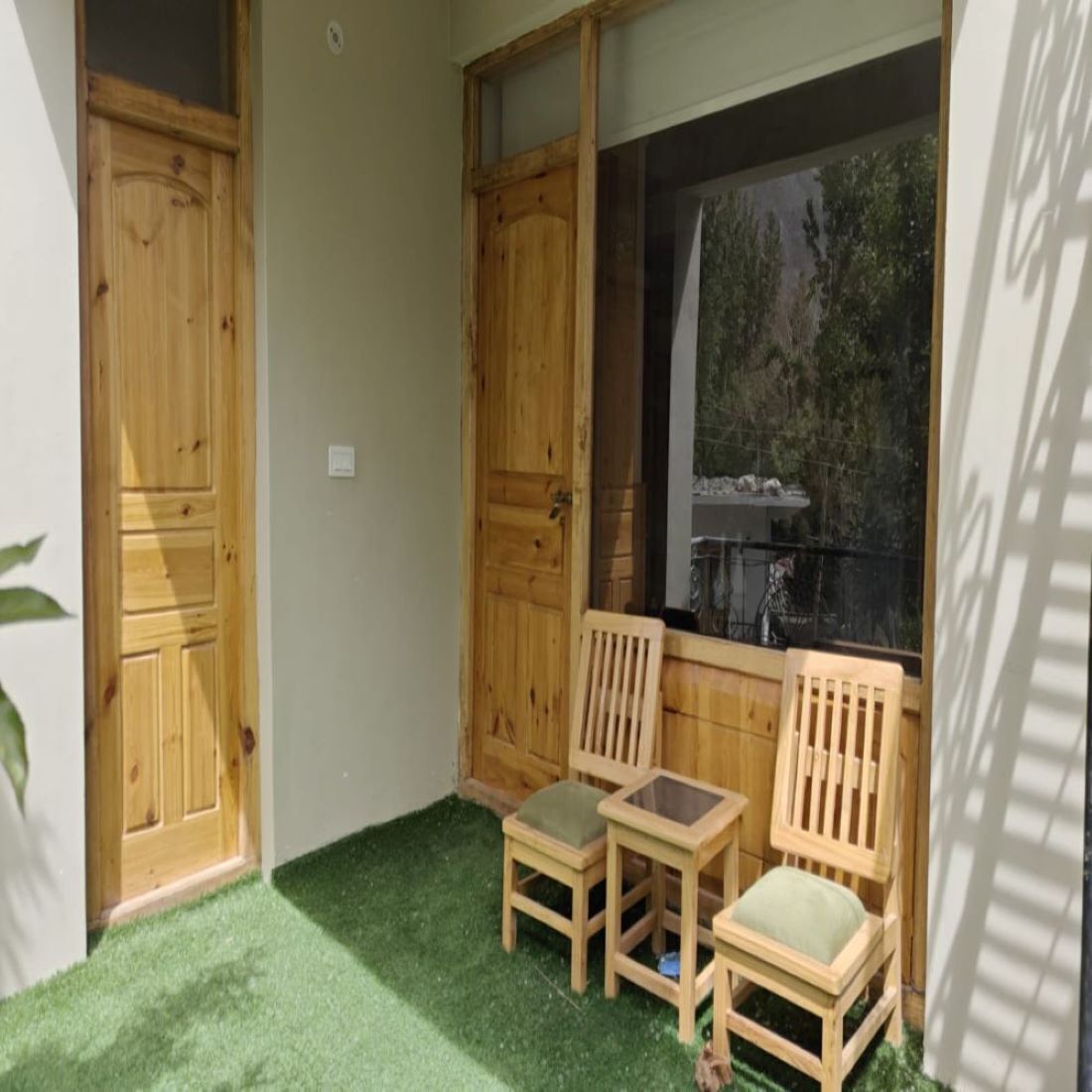 Habitación de esquina con dos puertas de madera, una ventana que da a árboles y dos sillones con cojines.