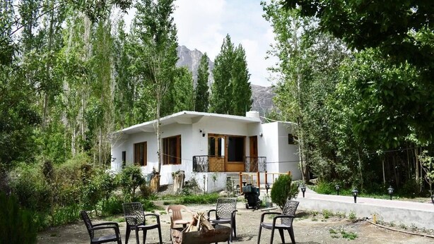 A white house with a balcony, surrounded by trees and a mountain in the background. - The Snowpeak Hunder (Hunder)