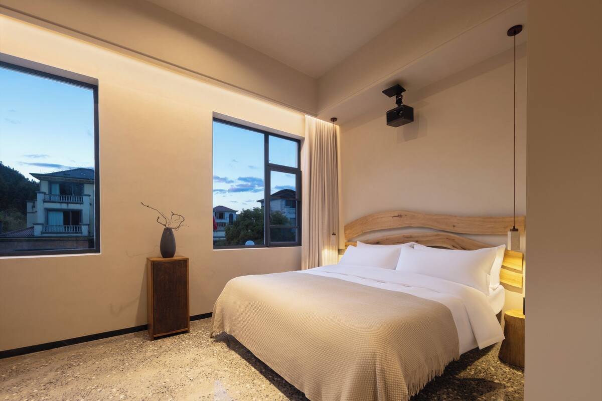 A bedroom with a large window, a wooden headboard, and a bedside lamp.