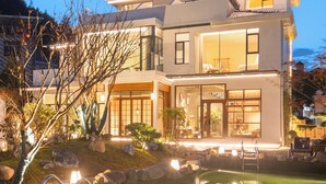 A modern two-story house with a large front yard, a pond, and a well-lit entrance. - Qingmo Hidden Mid-Mountain Hotel (Jingdezhen)