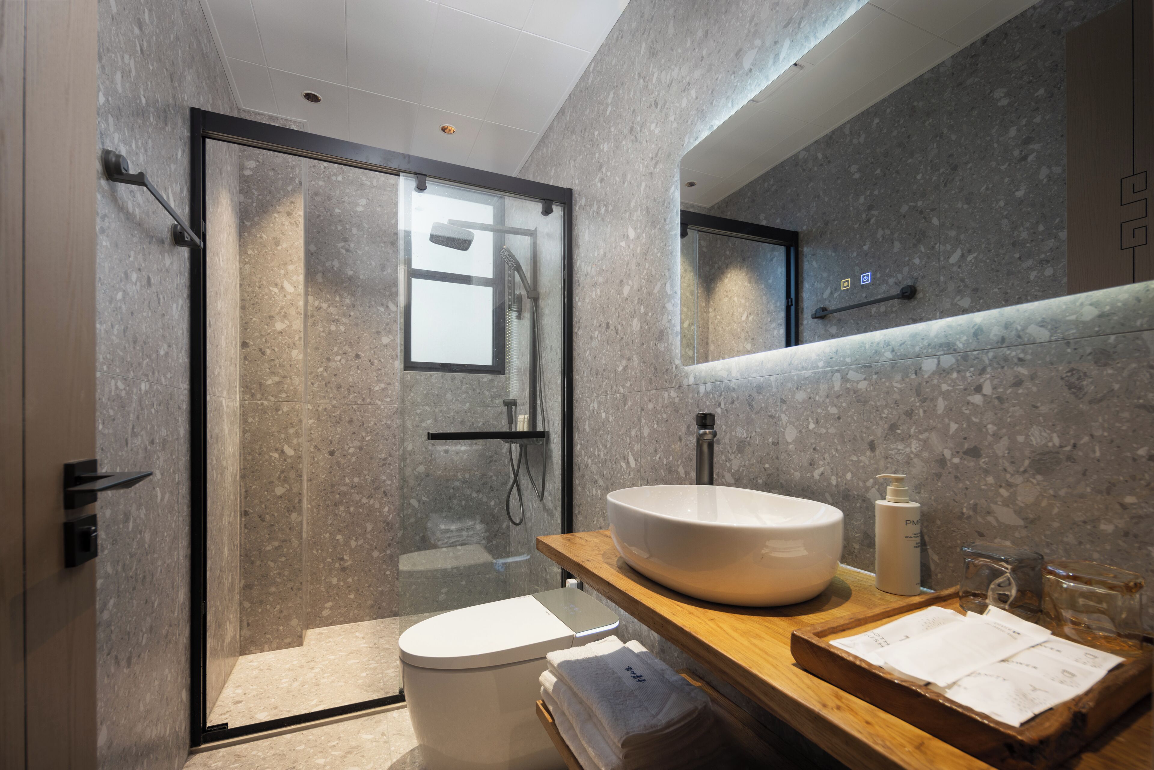 A modern bathroom with a glass-enclosed shower, a white toilet, a wooden vanity with a large sink, and a mirror above the vanity.