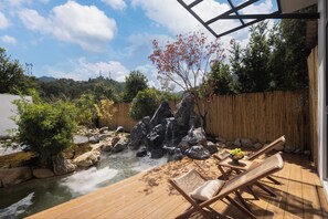 A wooden deck with a hot tub, surrounded by rocks and a bamboo fence. - Qingmo Hidden Mid-Mountain Hotel (Jingdezhen)