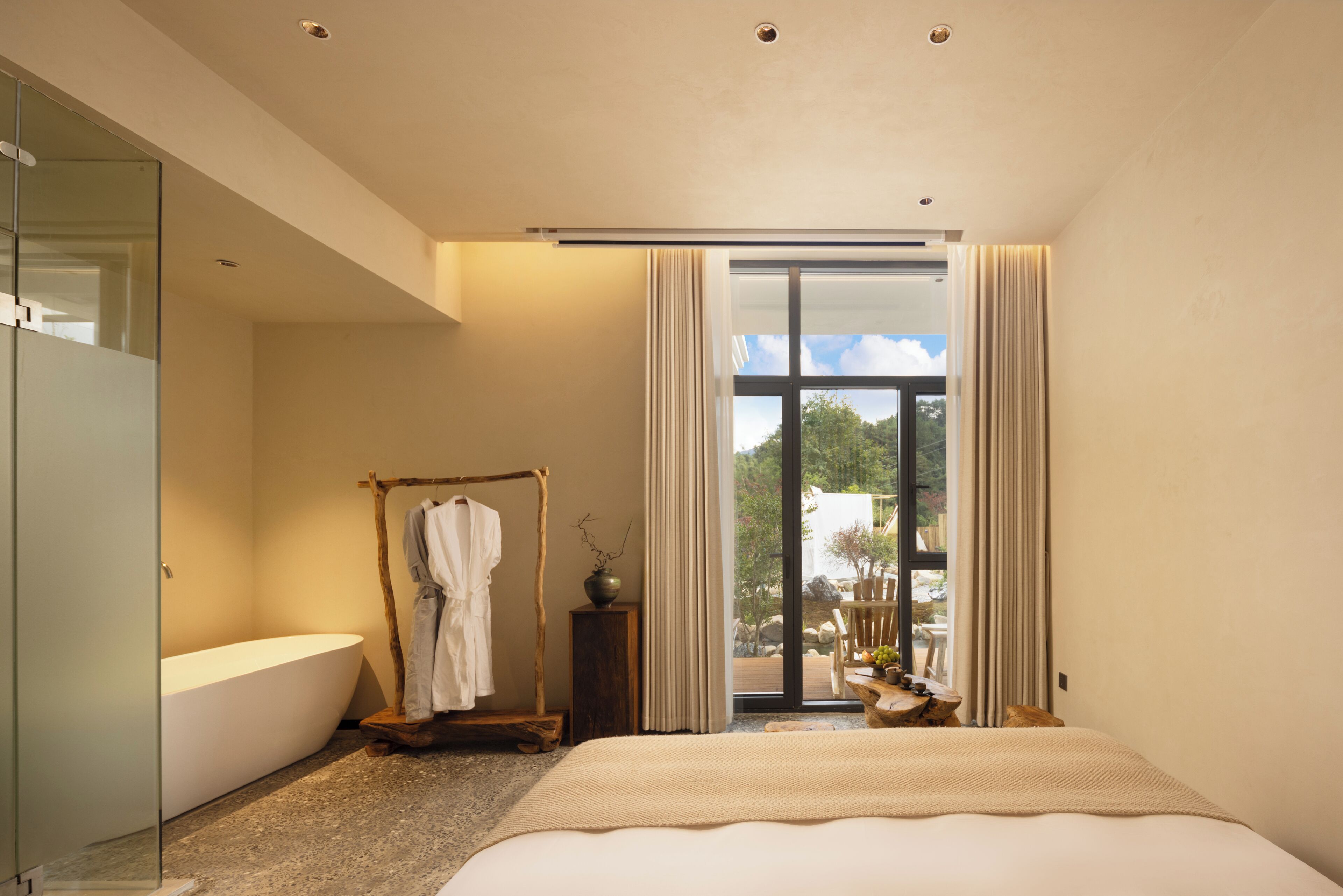 A modern bathroom with a freestanding bathtub, a wooden towel rack, and a large window offering a view of the outdoors.