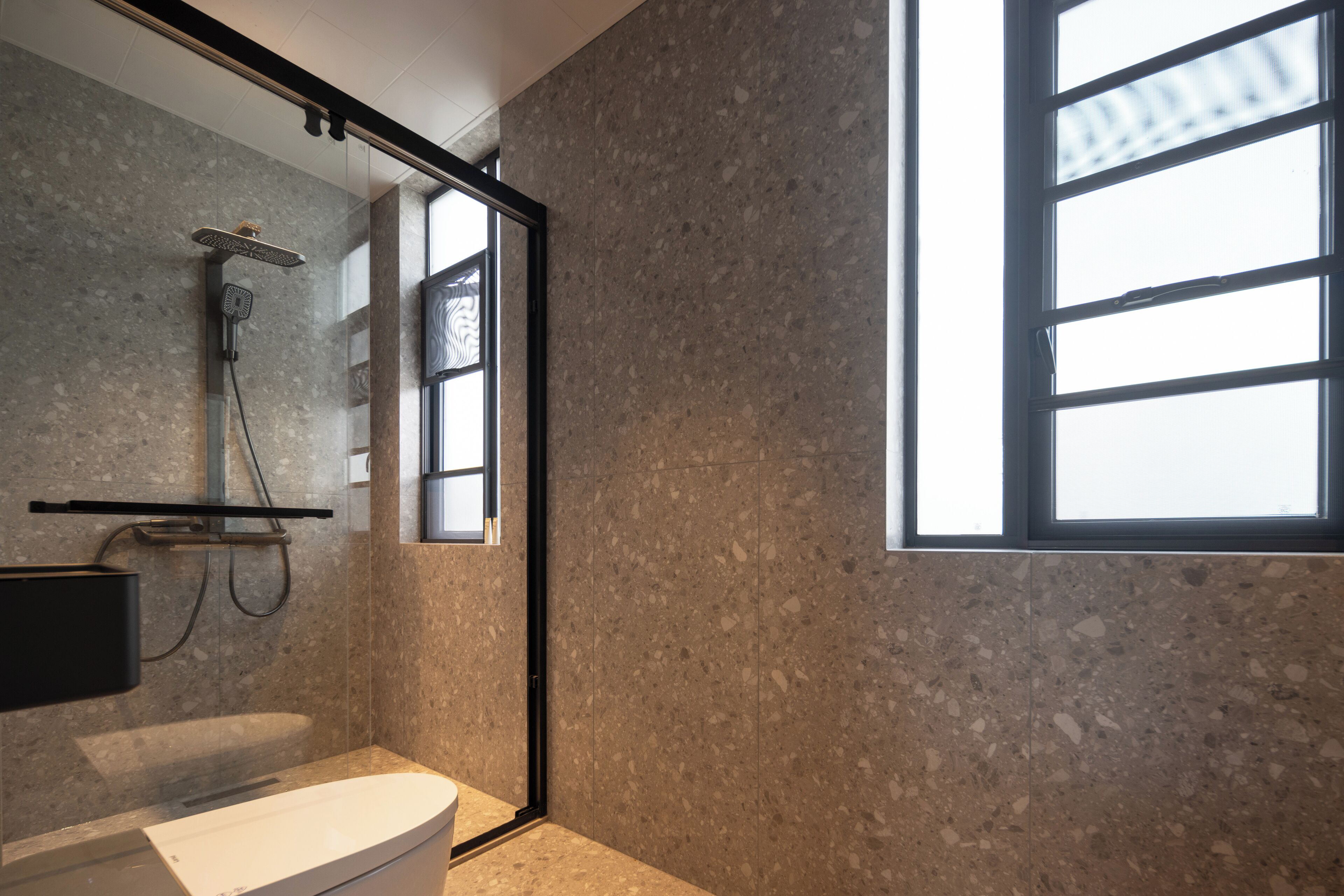A modern bathroom with a shower, toilet, and a large window providing natural light.