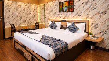 A hotel room with a large bed, wooden headboard, marble-patterned walls, a painting above the bed, a small side table, and a chair.