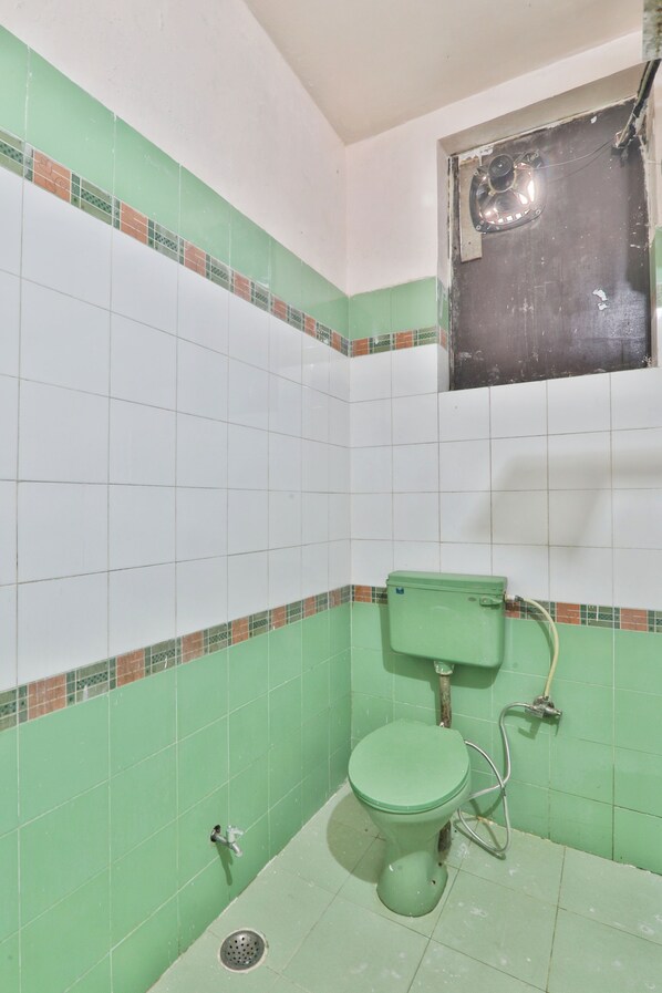 A bathroom with green and white tiles, a green toilet, and a window with a metal frame.