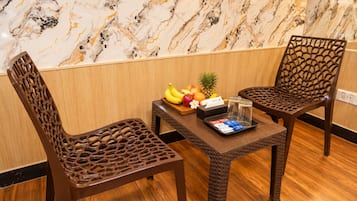 Una stanza con due sedie di legno, un tavolino con frutta e un vassoio di oggetti, e una parete decorata con effetto marmo.