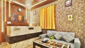 A reception area with a marble counter, a clock, a Buddha statue, and a sofa with cushions. - Hotel Kasol Heritage (Lucknow)