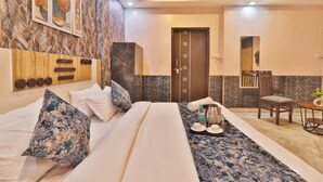 A hotel room with a large bed, a wooden headboard, a small table with a tray, a chair, and a door. - Hotel Kasol Heritage (Lucknow)