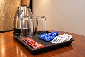 Un plateau avec une machine à café, deux verres et quelques en-cas emballés, posé sur une table en bois.