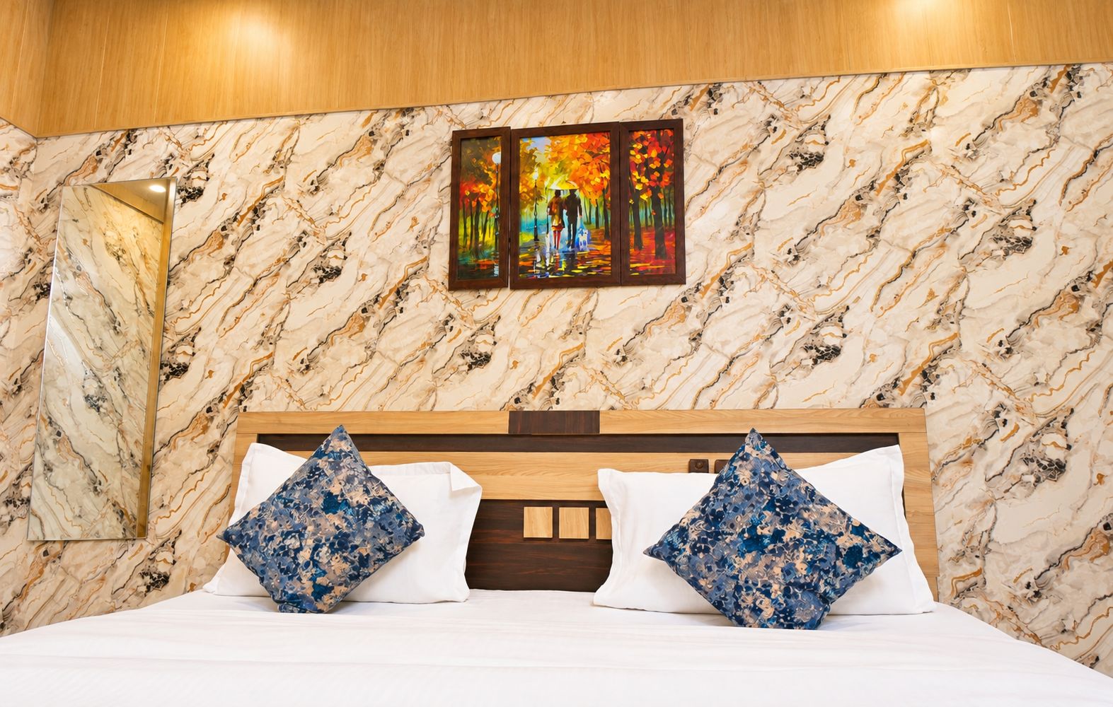 A hotel room with a marble-patterned wall, a bed with white bedding, and two decorative pillows.