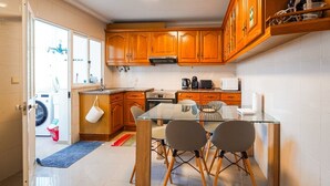 A compact kitchen with wooden cabinets, a glass dining table, and a built-in oven. - GuestReady - Machico Apartment with Balcony (Machico)