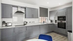 A modern kitchen with grey cabinets, a stainless steel range hood, a Bosch microwave, and a sink.
