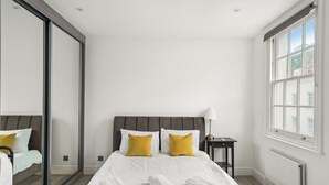 A hotel room with a large bed, two pillows, a nightstand, a lamp, and a window.