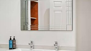 A modern bathroom with a large mirror, two sinks, and a white vanity.