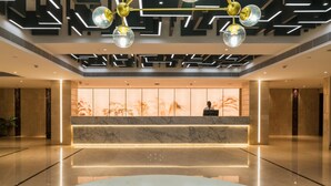 Un moderno vestíbulo de hotel con una recepción, suelo de mármol y diseño geométrico en el techo.