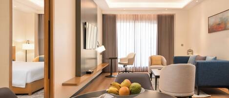 Une chambre d’hôtel avec un lit, une table à manger avec des fruits, un canapé et un téléviseur.