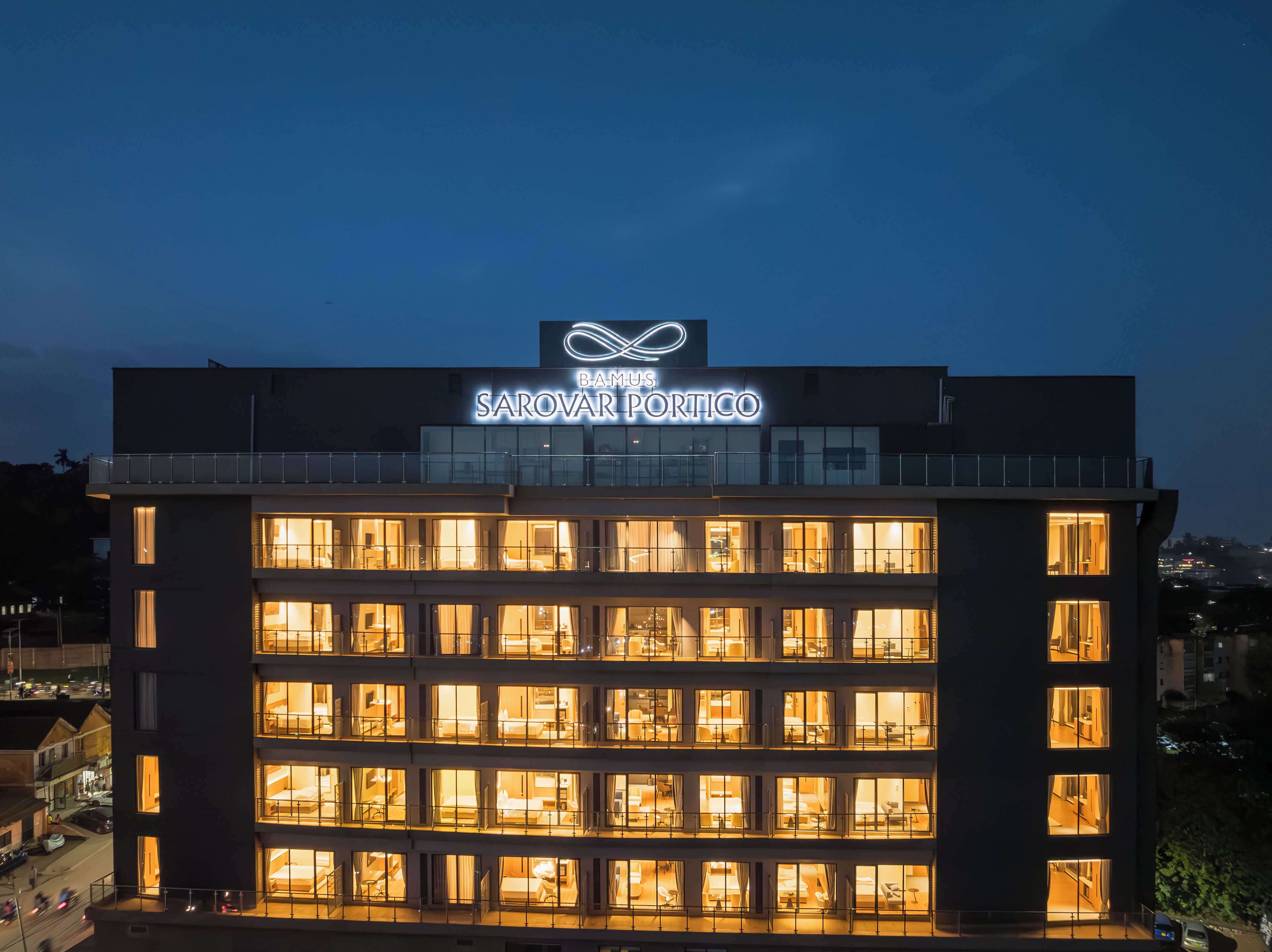 Un hôtel à plusieurs étages, avec des fenêtres illuminées et une enseigne indiquant « BAMUS SAROVAR PORTICO ».